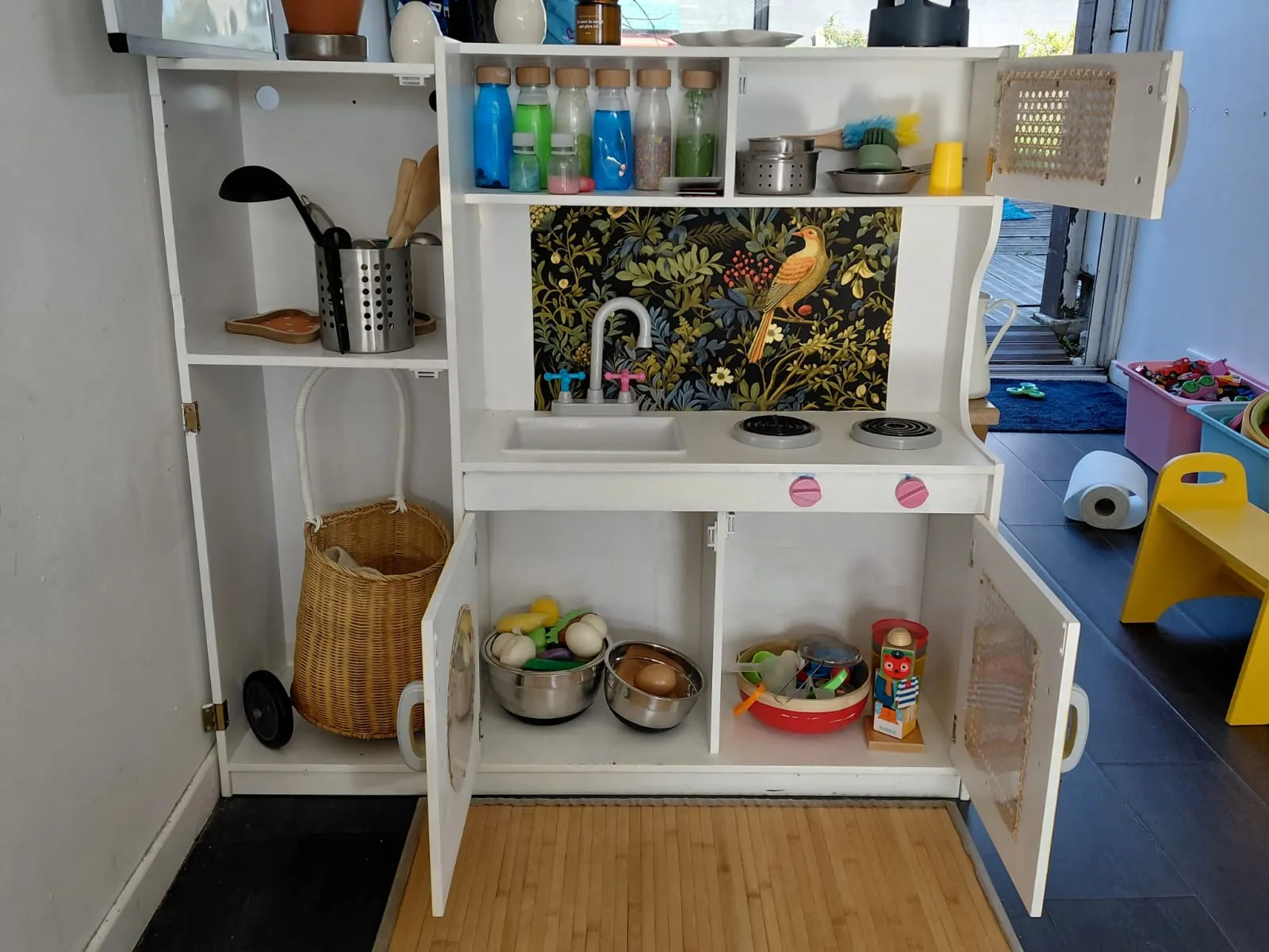 Coin cuisine symbolique de L'Escargotière — bouteilles sensorielles, ustensiles réels, pédagogie Montessori chez Sarah Poppins